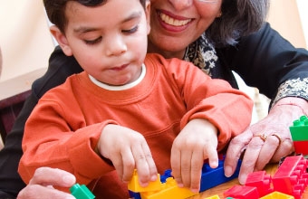 A child plays with blocks while his grandmother helps him