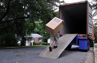 person carrying a moving box up a ramp into the back of a moving truck
